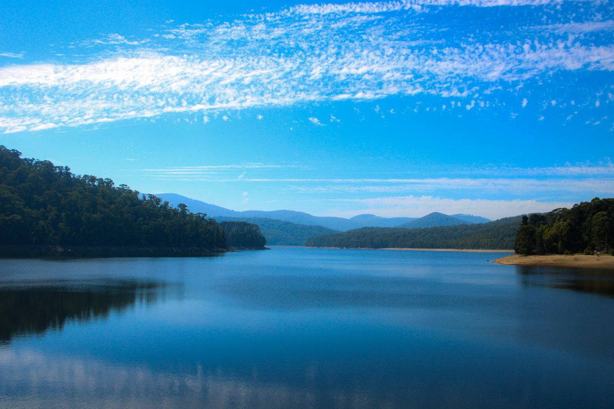 Calm blue lake framed by forested hills under a clear sky